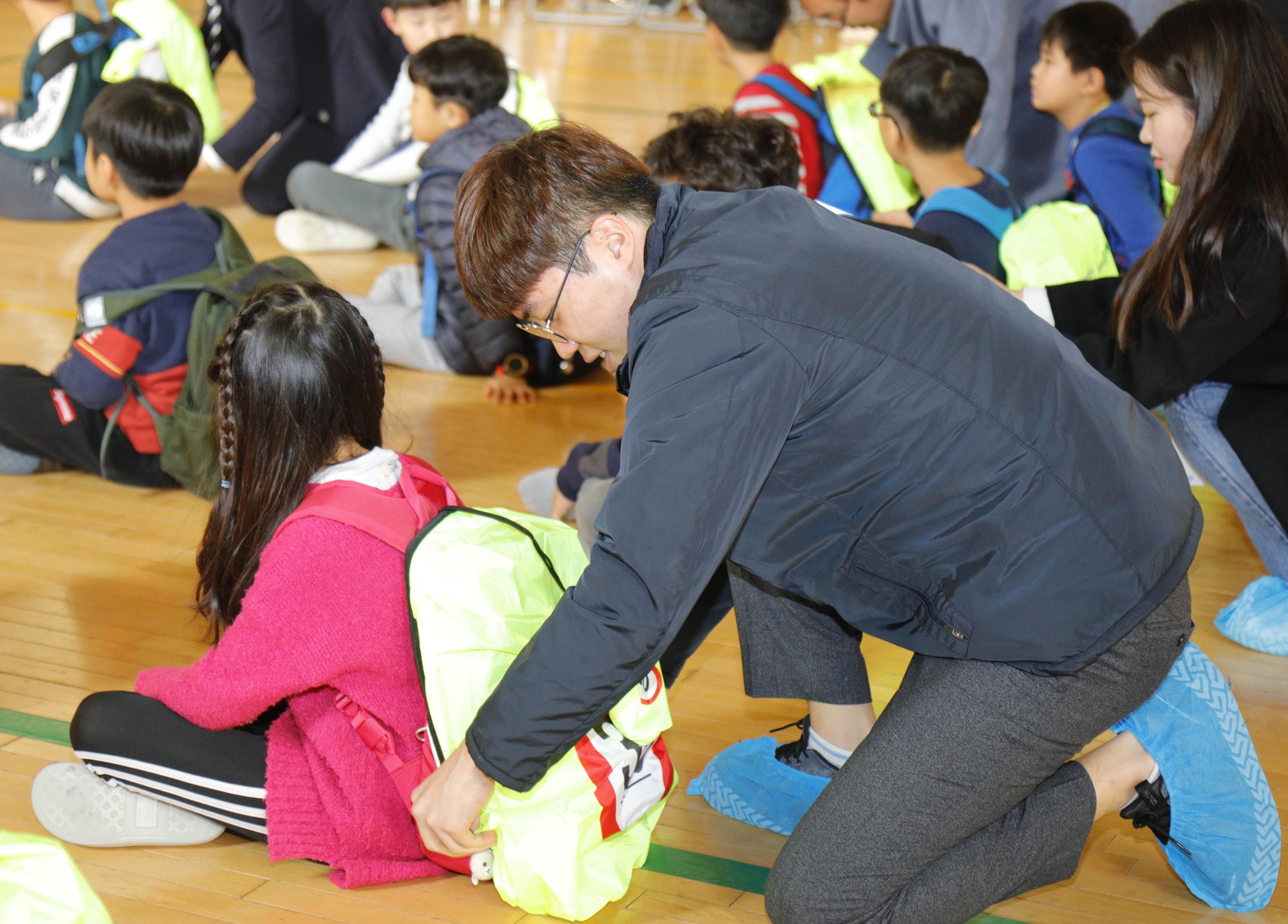 현대위아의 한 직원이 18일 경상남도 창원시 삼정자초등학교에서 한 학생의 가방에 교통사고 예방에 도움을 주는 ‘교통안전 가방덮개’를 씌우고 있다.